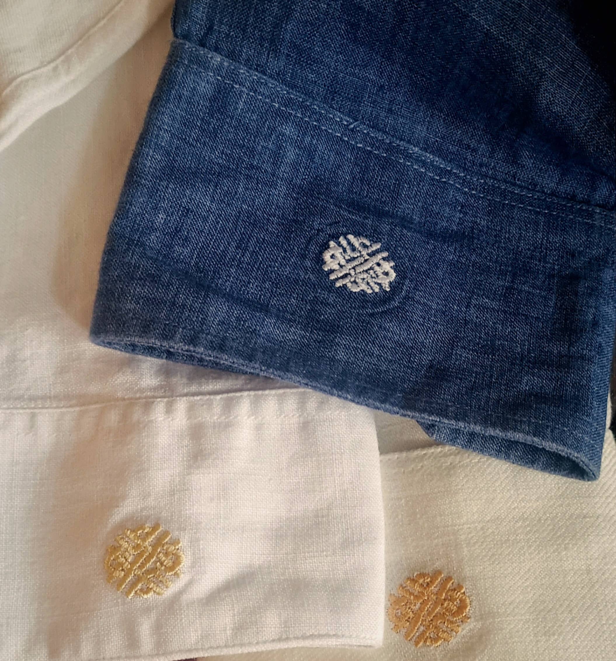 Three linen shirt cuffs, blue, white and ivory, each embroidered with the Quinta del Hilo emblem.