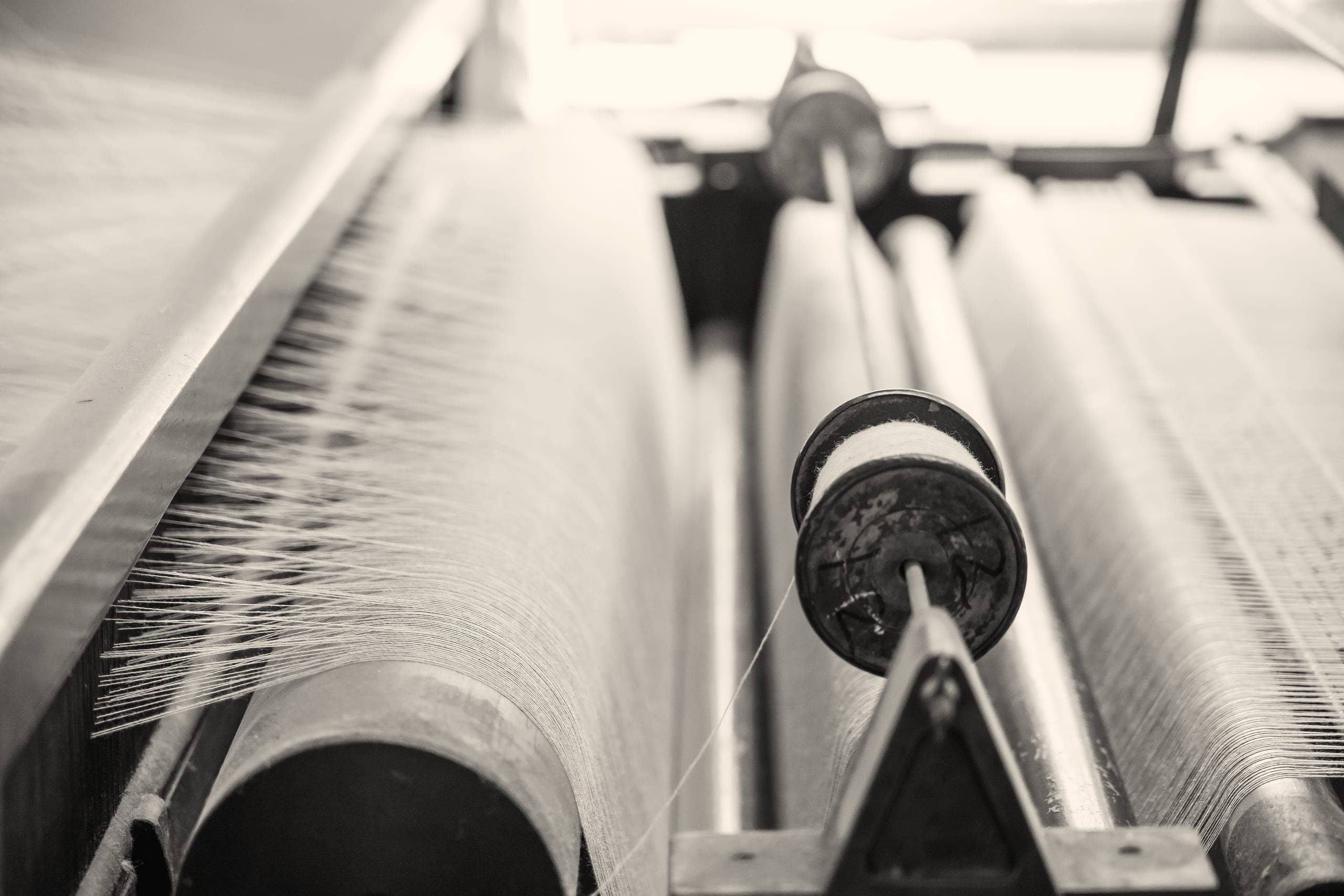 A bobbin of thread on a loom, beside the warp, in black and white