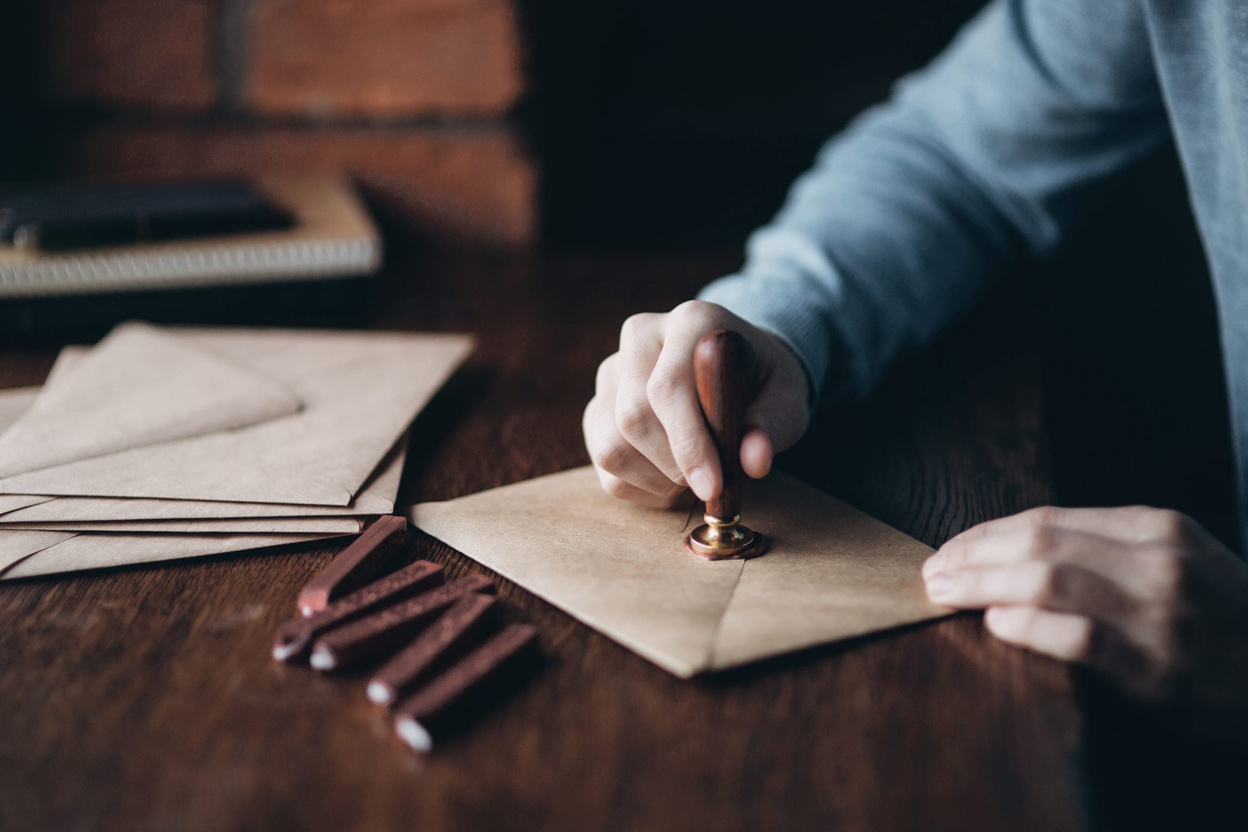 A hand pressing a brass seal stamp into wax on a kraft envelope